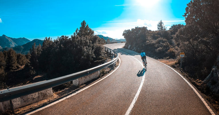 Syklist i blå trøye på vei opp på fjellet i Spania