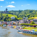 Utsikt over den historiske byen Cochem i Moseldalen med Mosel-elven, vinranker i forgrunnen og Reichsburg-slottet i bakgrunnen